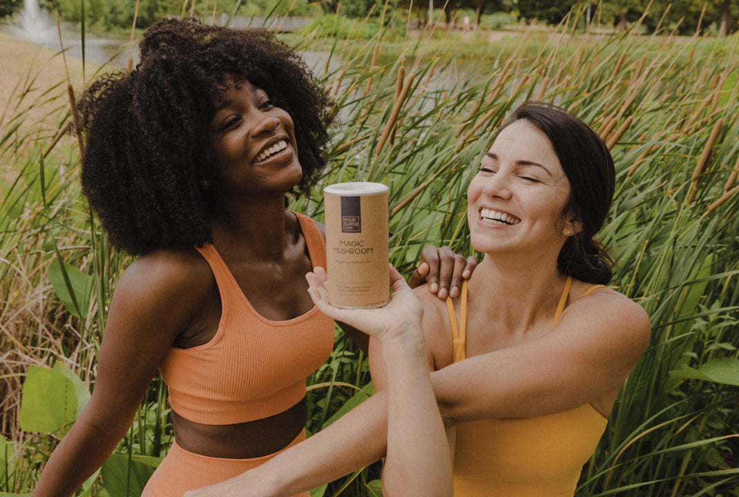 Two women in a field posing with a can of Your Super Magic Mushroom mix